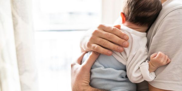 Ein junger Mann hält liebevoll ein Baby, das seinen Kopf auf seine Schulter legt – Symbol für sanfte Pflege mit Tannosynt bei Windeldermatitis.